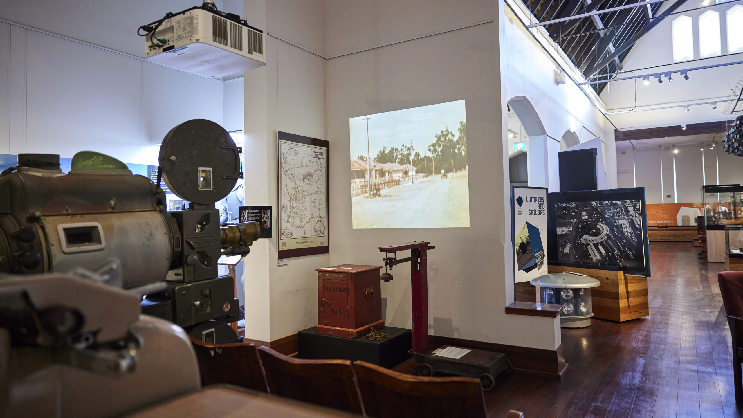 Inside of the museum featuring an old film projector projecting old footage of a homestead on to a wall. Display cabinets with artefacts and museum signgage.