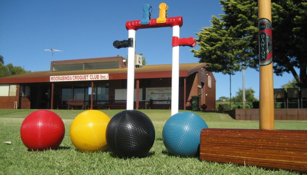 Four coloured croquet balls and a croquet mallet in front of the club building.