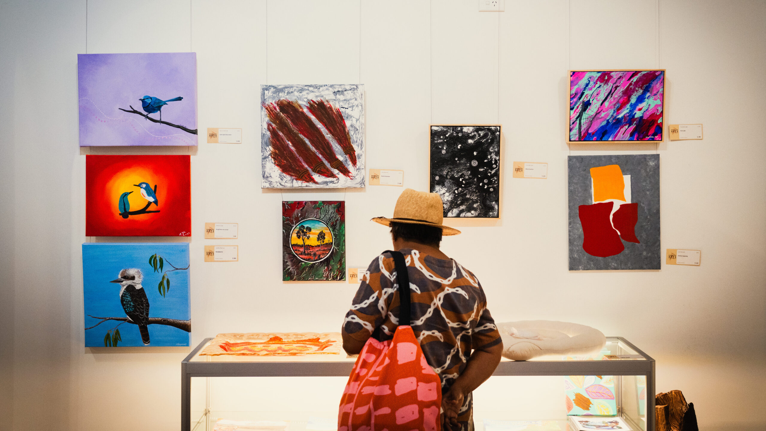 Person looking at colorful paintings displayed on a wall in a gallery.